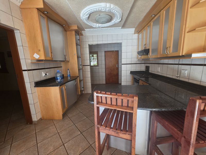A functional kitchen featuring wooden cabinetry, granite countertops, a built-in hob with extractor fan, and tiled flooring with a decorative ceiling rose.