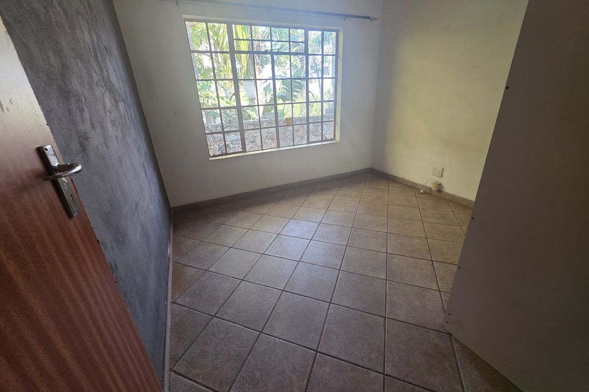 An empty bedroom featuring tiled flooring, a large grid-pattern window, and an unfinished accent wall, offering a blank canvas for renovation.