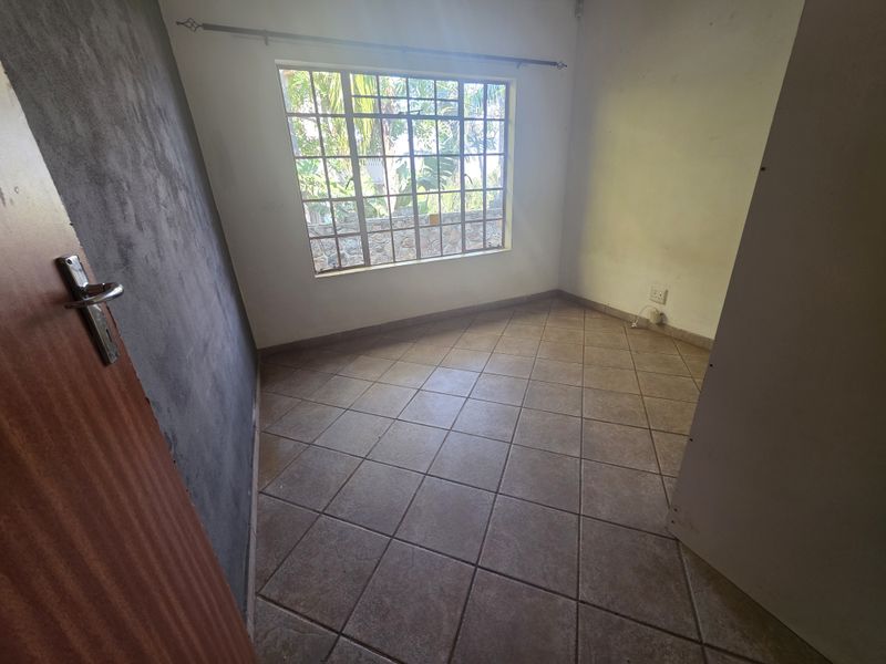 An empty bedroom featuring tiled flooring, a large grid-pattern window, and an unfinished accent wall, offering a blank canvas for renovation.