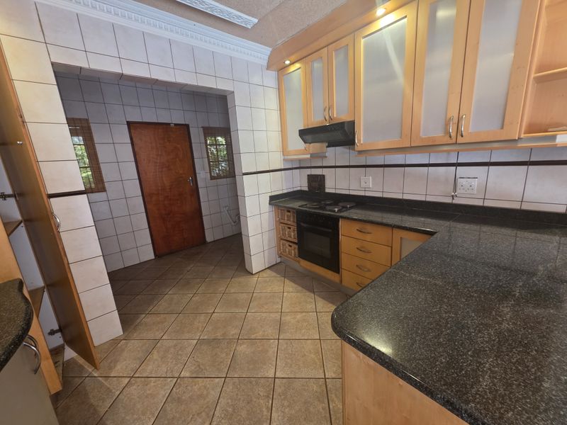 A functional kitchen featuring granite countertops, wooden cabinetry, built-in oven and hob, and tiled finishes throughout.