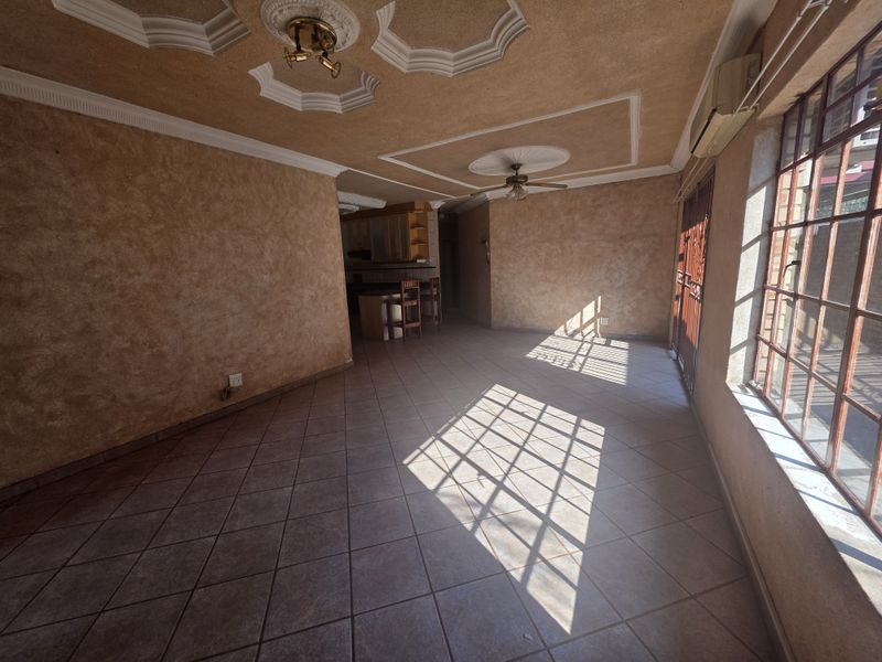 Spacious open-plan living area featuring tiled floors, decorative ceiling details, a ceiling fan, and an integrated air conditioning unit with natural light.