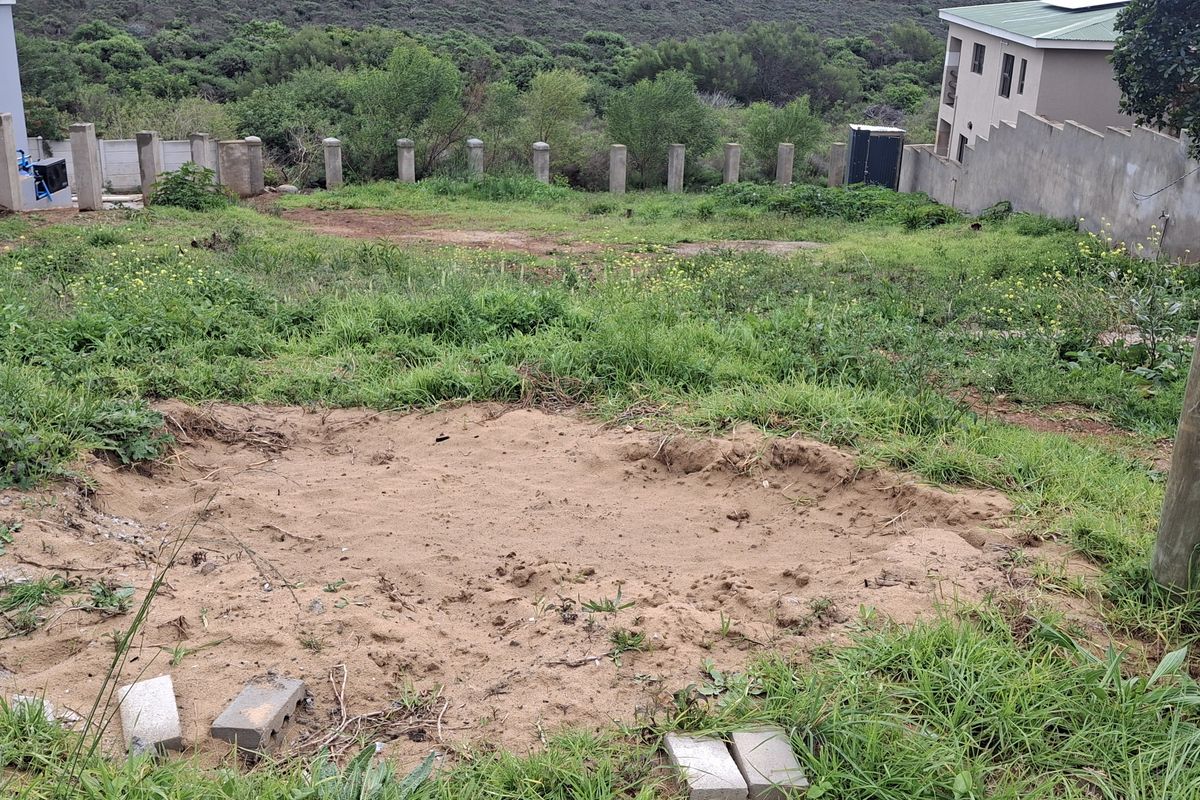 A view of a vacant residential plot featuring a sloped landscape, boundary walls, and existing concrete structural pillars.