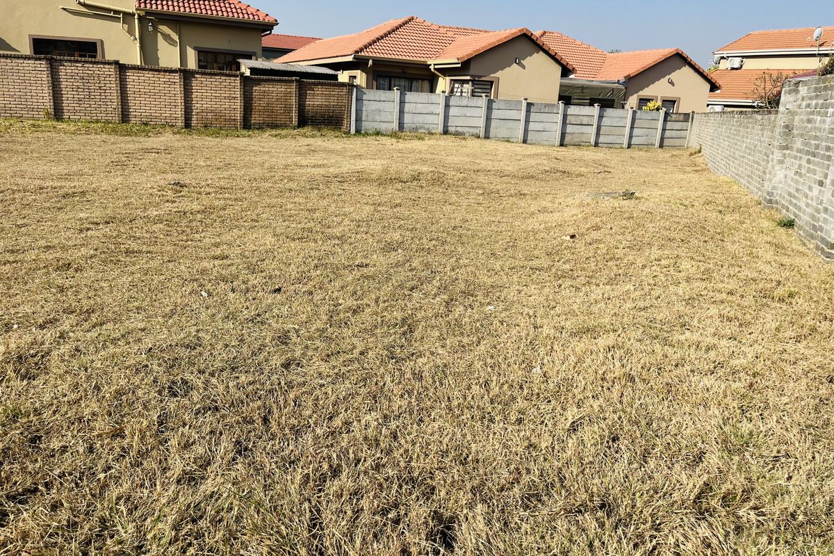 A vacant residential plot featuring dry grass and enclosed by perimeter brick and concrete boundary walls.