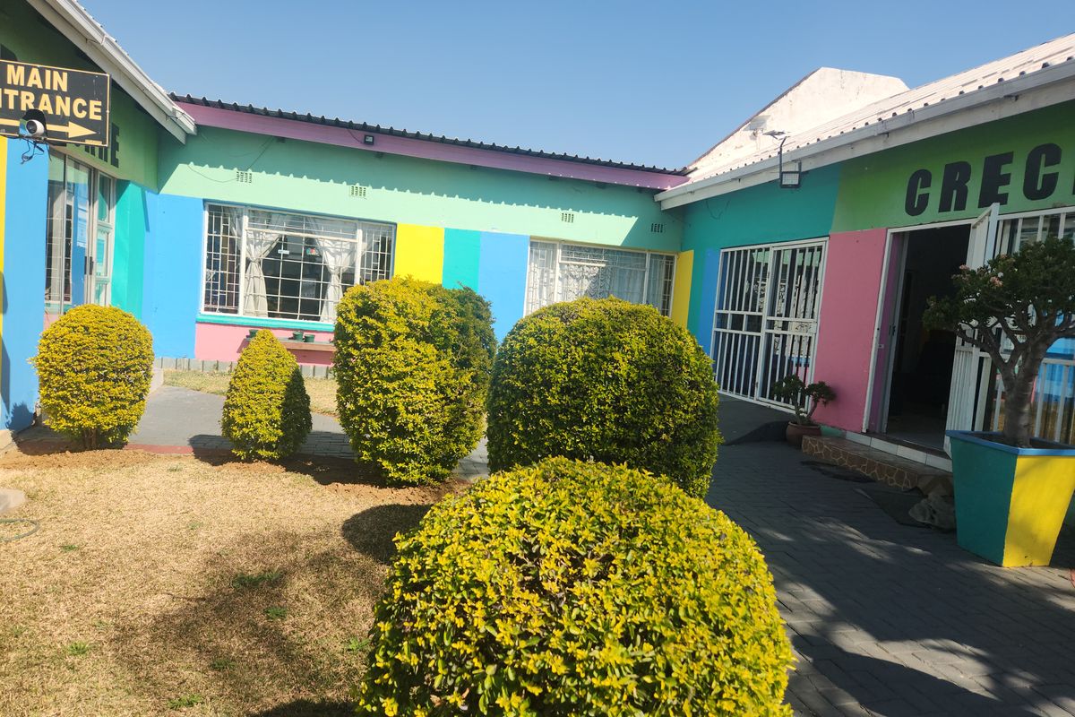 Exterior view of a commercial or educational property featuring a paved courtyard, security gates, and colorful exterior wall finishes.