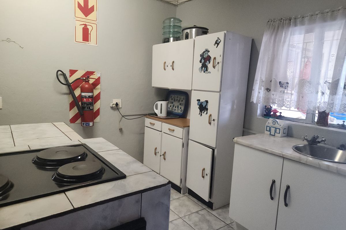 A functional kitchen featuring tiled countertops, an electric hob, built-in cabinetry, and a stainless steel sink with security bars on the window.