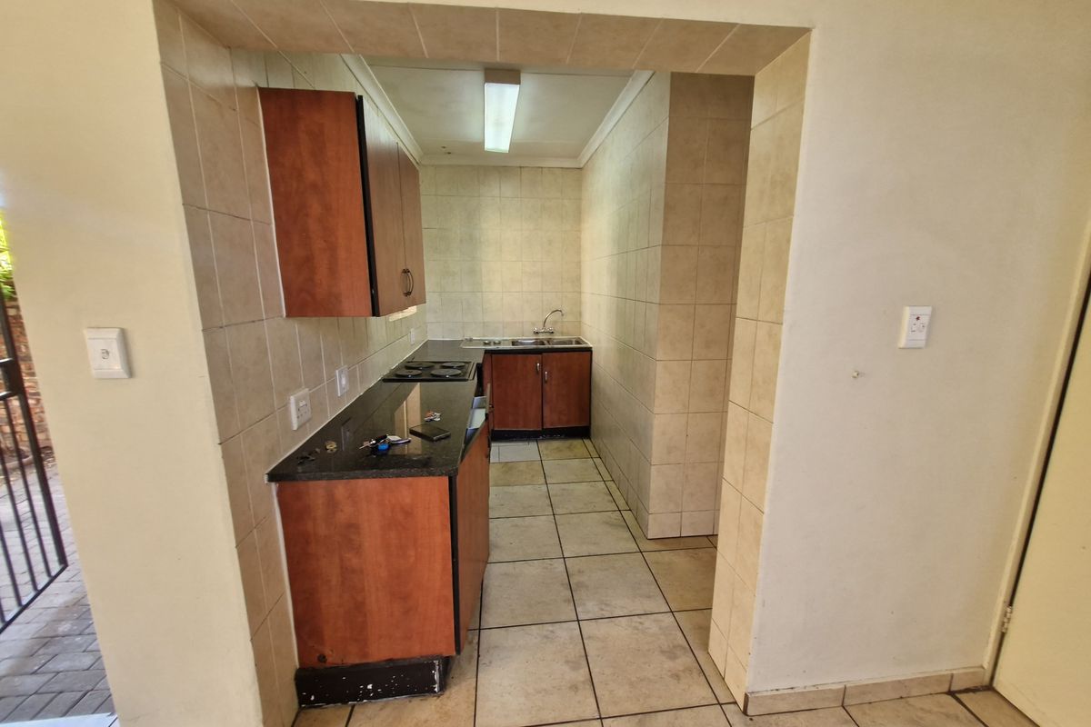 A compact, functional kitchen featuring built-in wooden cabinetry, granite countertops, a hob, and a double sink with tiled finishes throughout.
