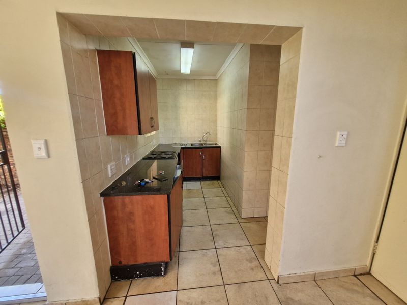 A compact, functional kitchen featuring built-in wooden cabinetry, granite countertops, a hob, and a double sink with tiled finishes throughout.