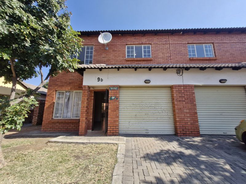 Front elevation of a face brick townhouse featuring a double garage, paved driveway, and established garden area.