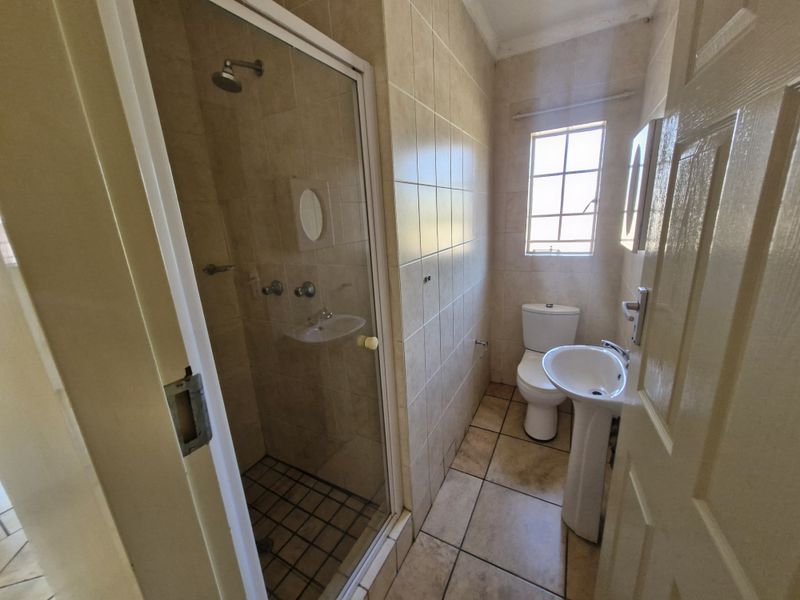A functional bathroom featuring a shower enclosure, pedestal basin, and toilet with neutral wall and floor tiling.