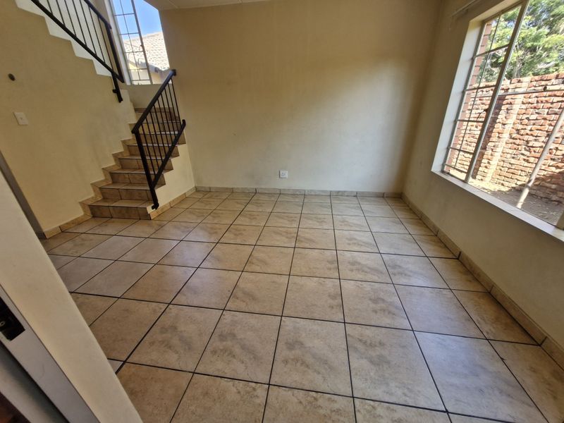 An empty living area featuring tiled flooring, a staircase with a metal railing, and large windows allowing natural light.