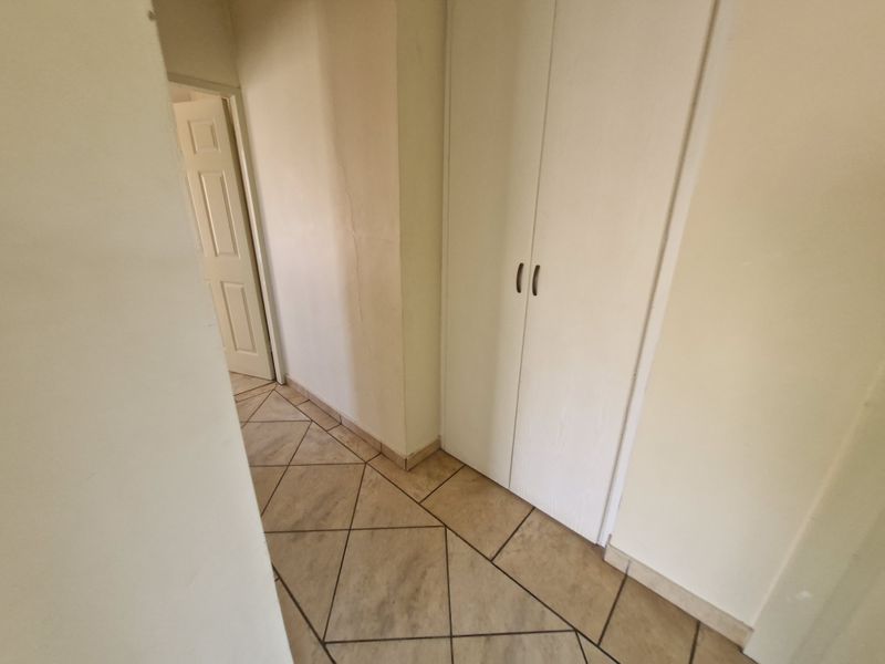 A functional hallway featuring tiled flooring and a built-in storage cupboard, providing access to adjacent rooms.