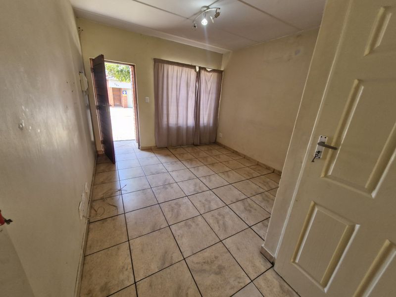 An empty living room featuring tiled flooring, neutral walls, and direct access to the exterior through a doorway.