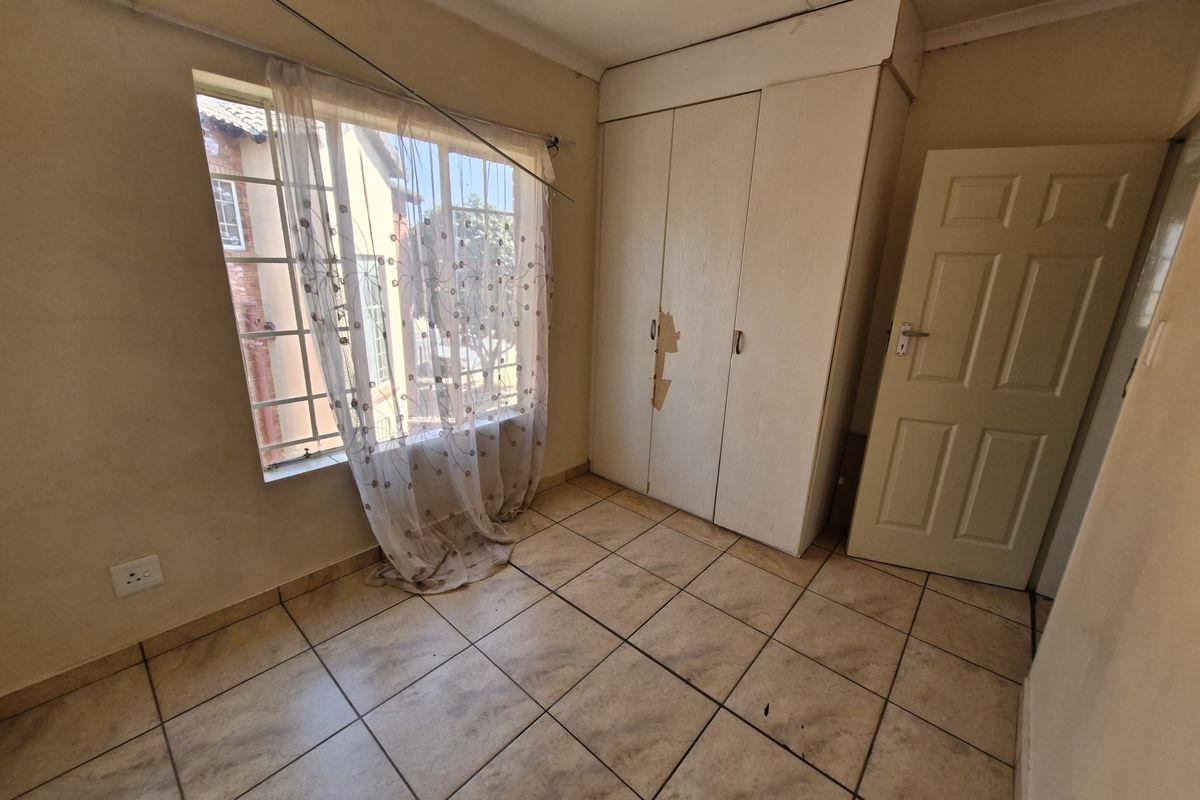 An empty bedroom featuring tiled flooring, a built-in wardrobe with visible surface damage, and a window fitted with security bars.