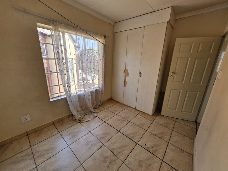 An empty bedroom featuring tiled flooring, a built-in wardrobe with visible surface damage, and a window fitted with security bars.