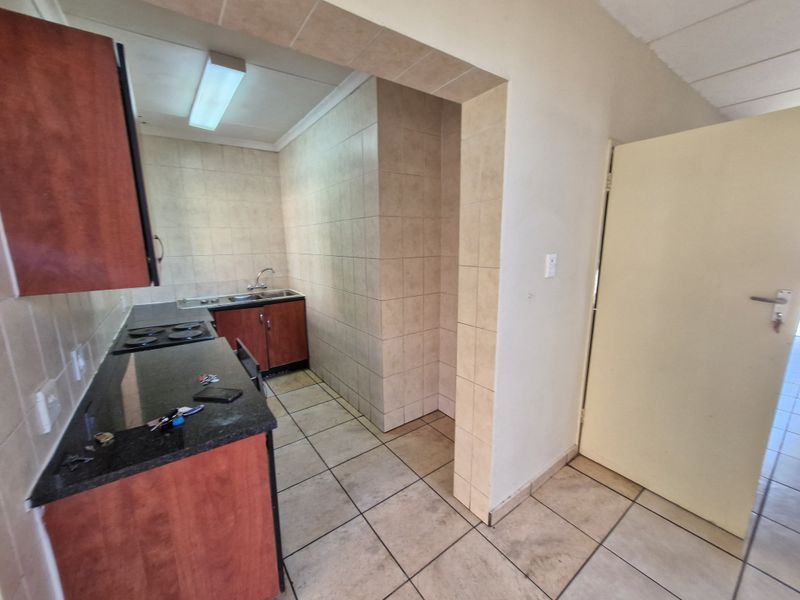 A functional kitchen featuring built-in cabinetry, granite countertops, an electric hob, and tiled finishes throughout.