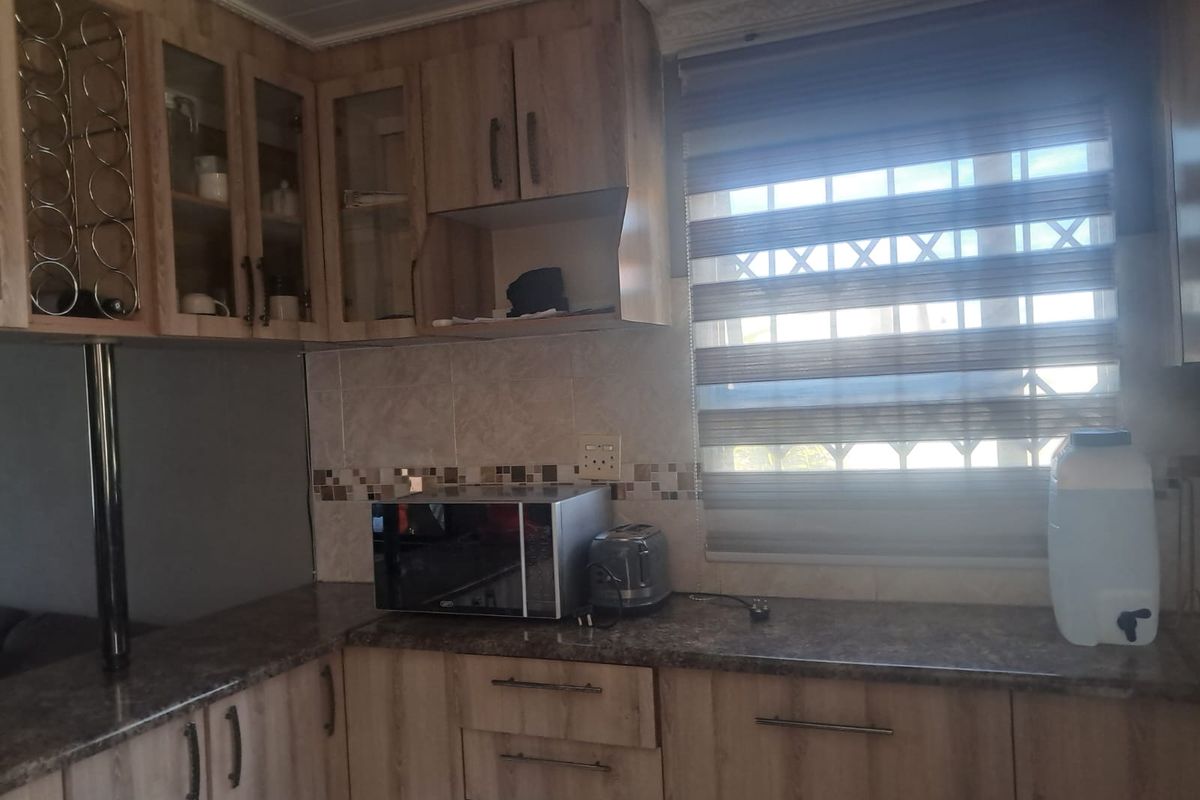 A functional kitchen featuring wood-look laminate cabinetry, stone-patterned countertops, and a tiled backsplash with a window providing natural light.