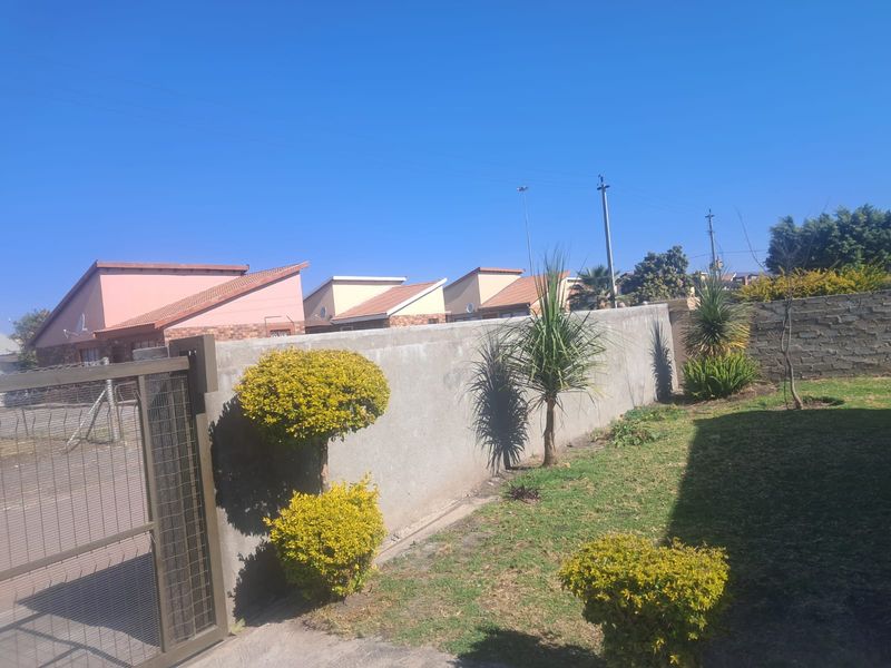 A view of the rear garden area featuring a perimeter wall, metal gate, and established lawn with surrounding residential properties.