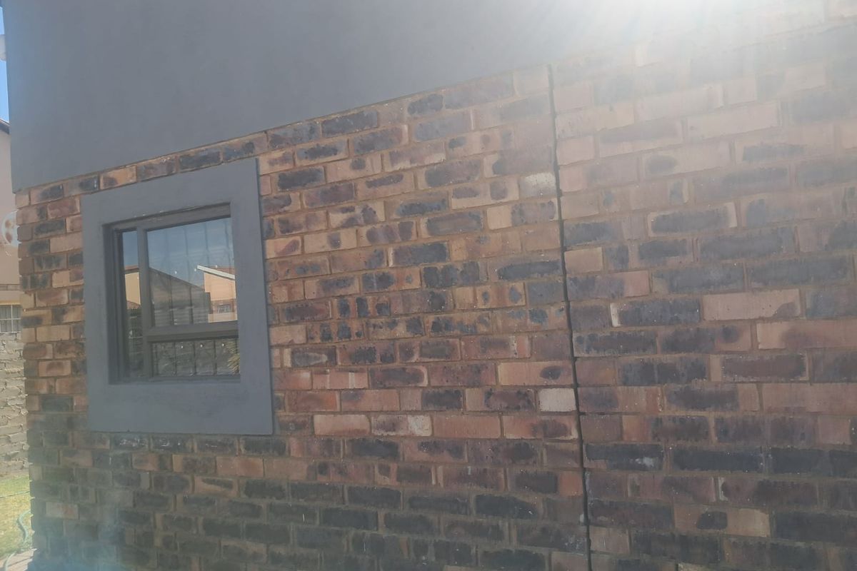 A view of the exterior rear wall featuring face brick construction, a sliding window, and a visible vertical crack in the masonry.