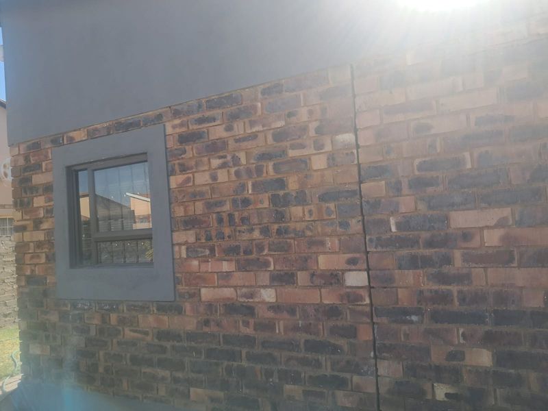 A view of the exterior rear wall featuring face brick construction, a sliding window, and a visible vertical crack in the masonry.