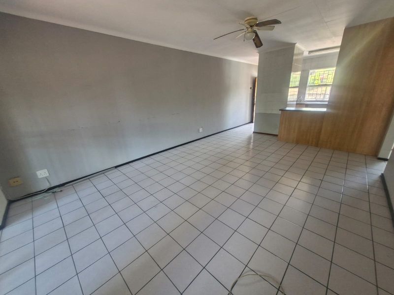 An open-plan living and kitchen area featuring tiled flooring, a ceiling fan, and a breakfast bar, currently vacant and ready for renovation.