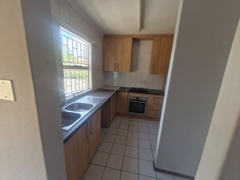 A functional kitchen featuring built-in wooden cabinetry, a double sink, and integrated oven and hob, with tiled flooring and natural light.