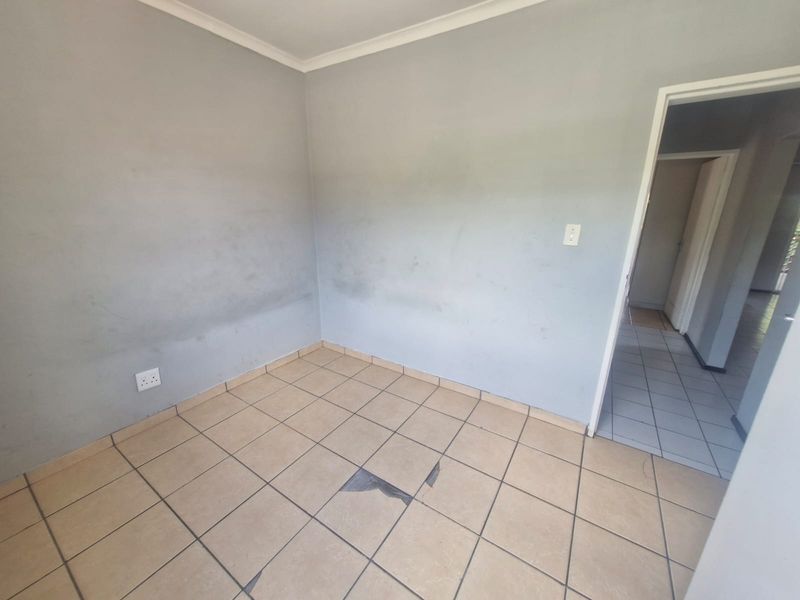 An empty bedroom featuring ceramic floor tiles and neutral wall finishes, requiring minor repairs to the flooring and paintwork.
