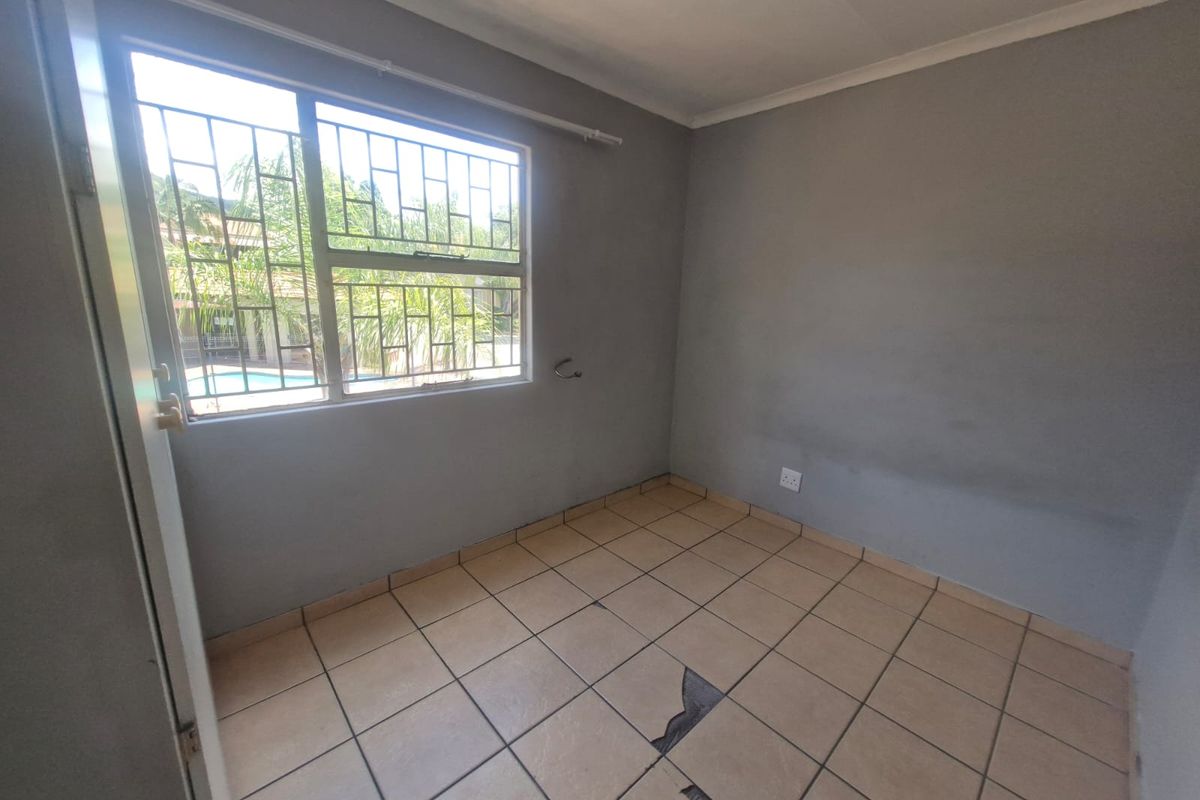 An empty bedroom featuring tiled flooring with visible damage and security bars on the window.