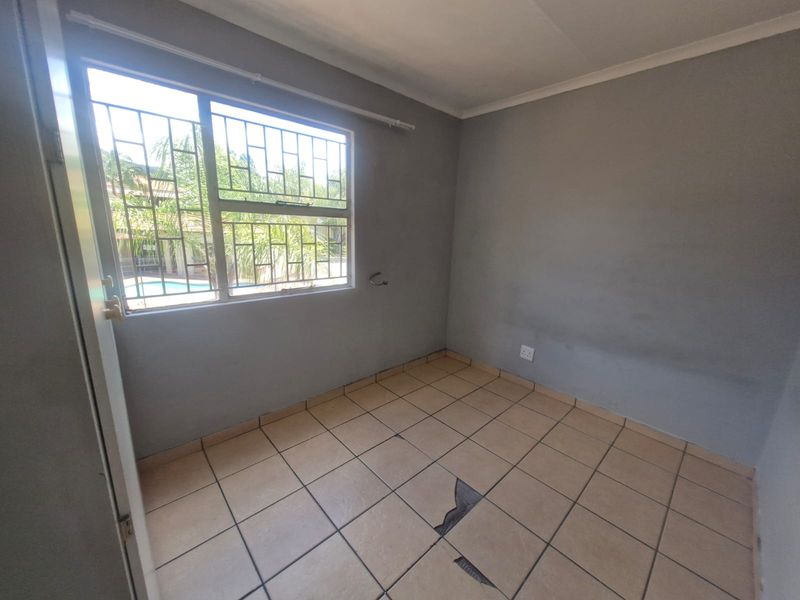 An empty bedroom featuring tiled flooring with visible damage and security bars on the window.