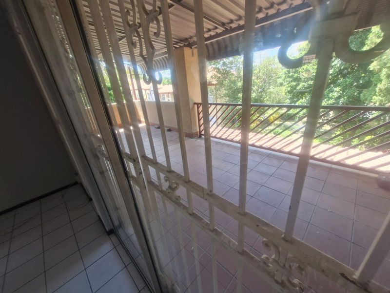 A covered balcony featuring tiled flooring and metal security gate, offering an outdoor space with views of the surrounding greenery.