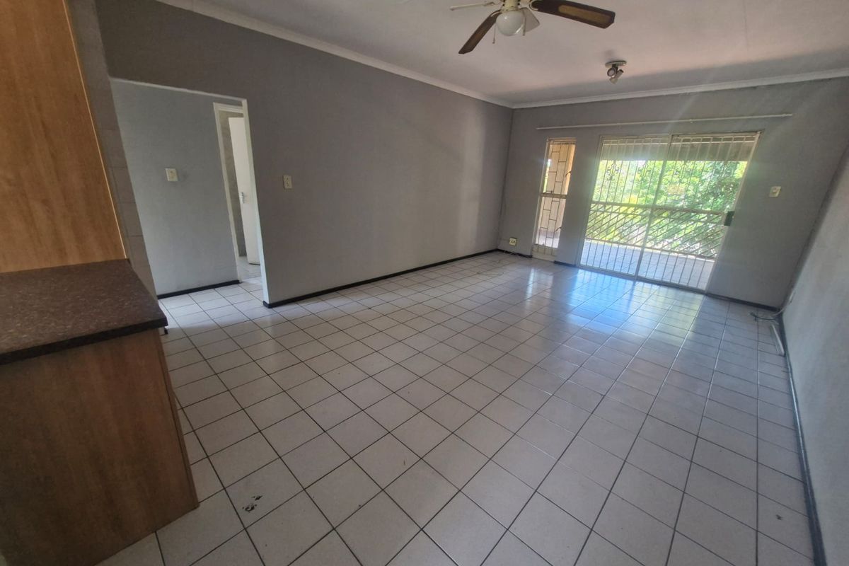 Spacious open-plan living area featuring tiled flooring, a ceiling fan, and direct access to a balcony through sliding glass doors.
