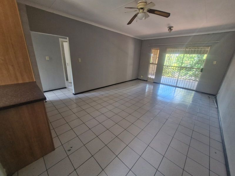 Spacious open-plan living area featuring tiled flooring, a ceiling fan, and direct access to a balcony through sliding glass doors.