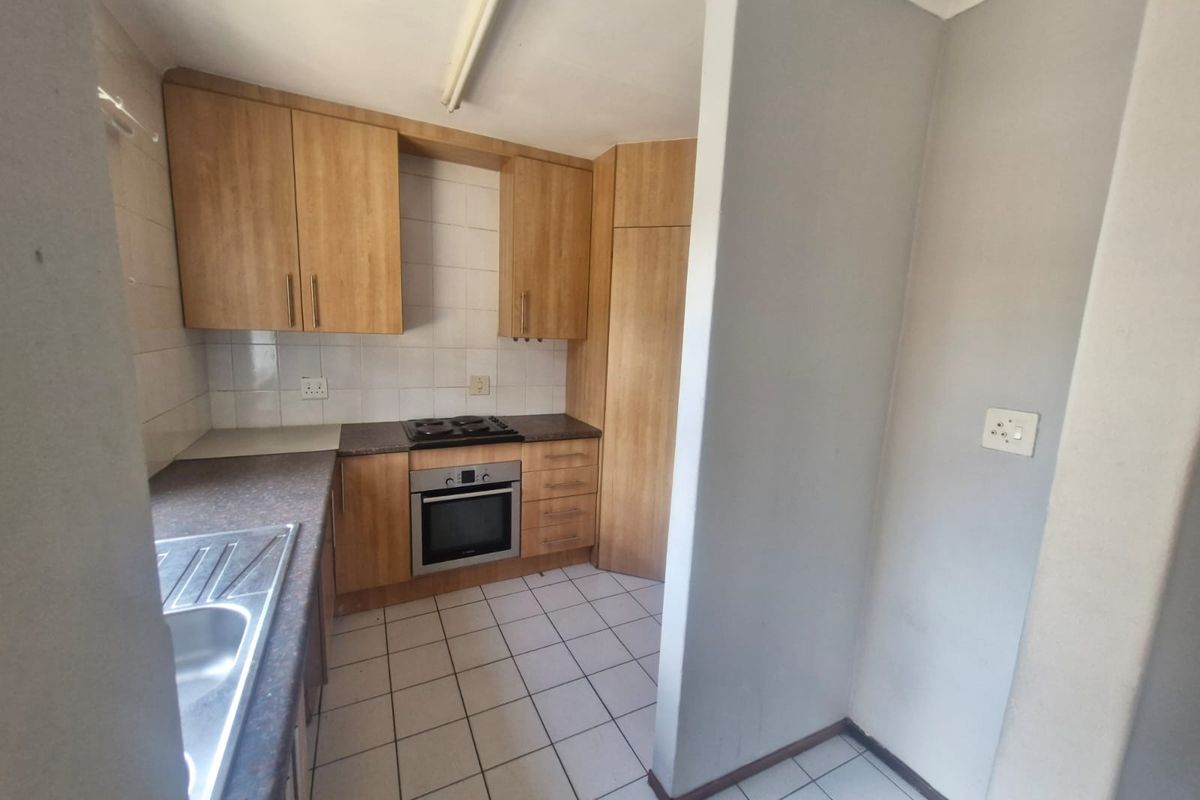 A functional kitchen featuring wood-look cabinetry, built-in oven and hob, tiled backsplash, and tiled flooring, offering a clean canvas for potential updates.
