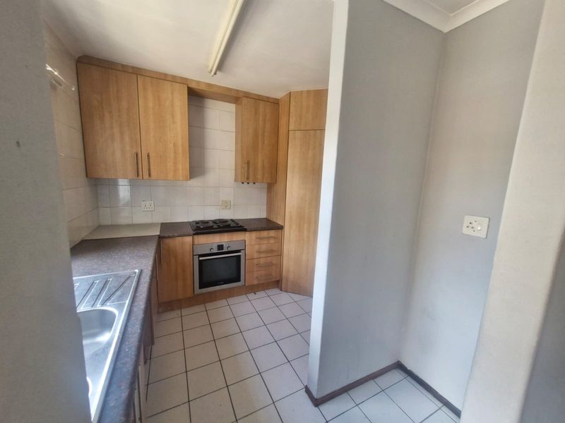 A functional kitchen featuring wood-look cabinetry, built-in oven and hob, tiled backsplash, and tiled flooring, offering a clean canvas for potential updates.
