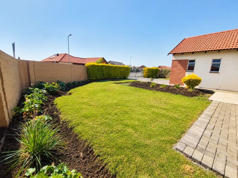 A well-maintained rear garden featuring a manicured lawn, landscaped garden beds, a paved walkway, and a secure boundary wall.