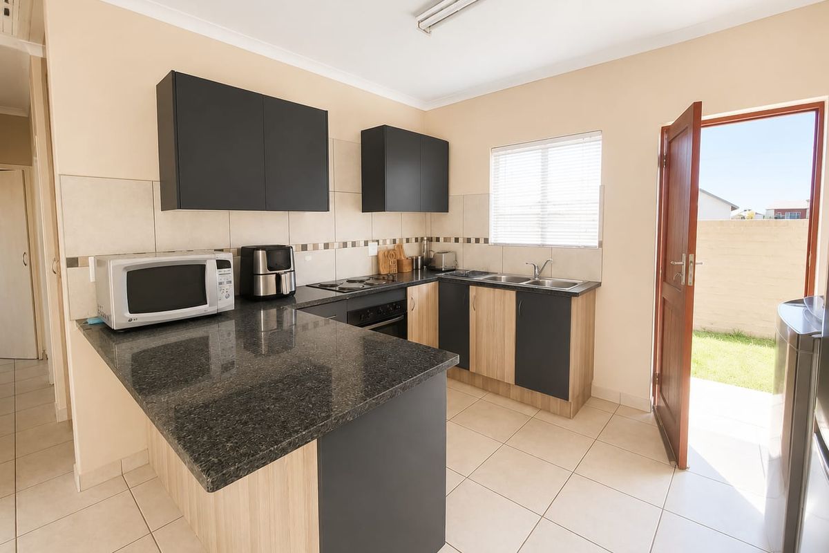 A functional kitchen featuring granite countertops, built-in oven, electric hob, double sink, and modern two-tone cabinetry with direct access to the rear garden.