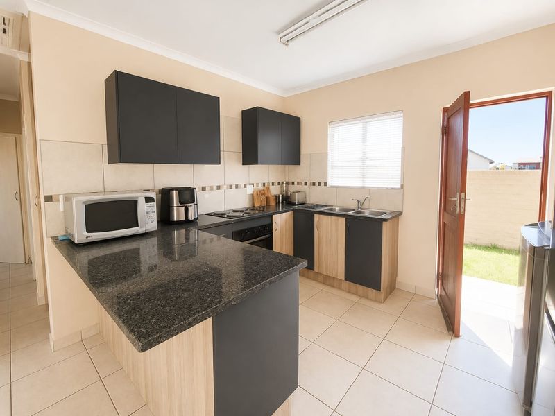 A functional kitchen featuring granite countertops, built-in oven, electric hob, double sink, and modern two-tone cabinetry with direct access to the rear garden.