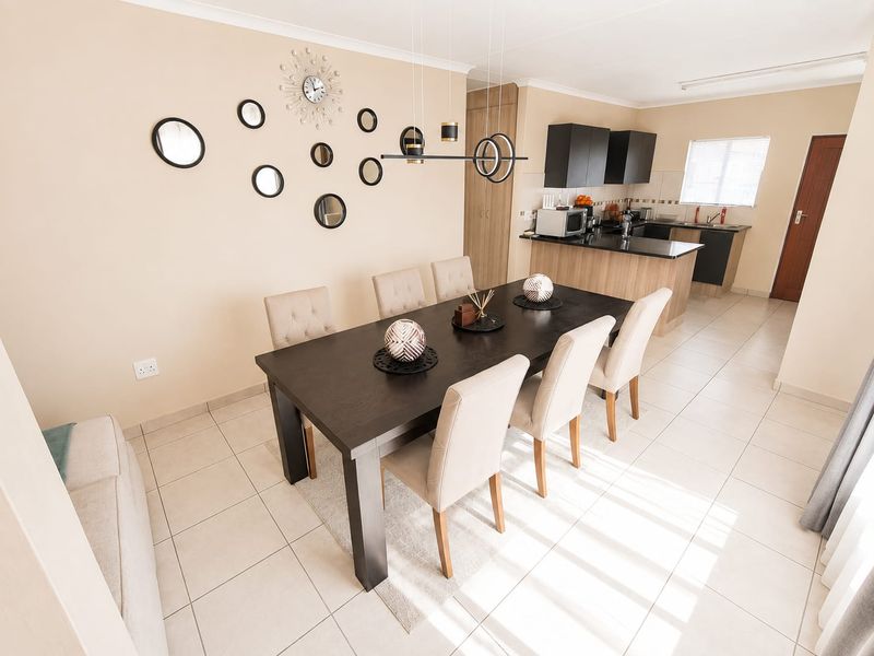 Open-plan dining area flowing into a functional kitchen with dark cabinetry, granite countertops, and tiled flooring throughout.