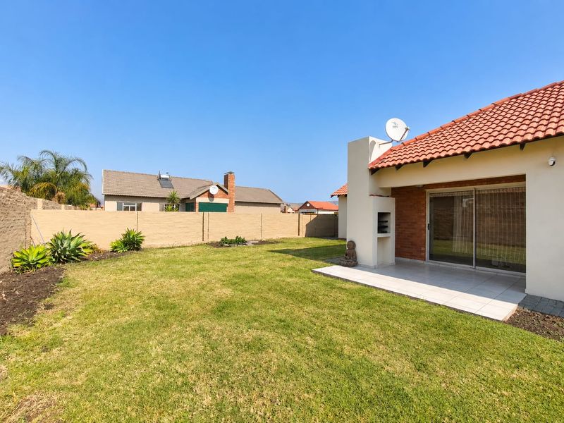 Rear garden featuring a paved patio area with a built-in braai and sliding door access to the townhouse interior.
