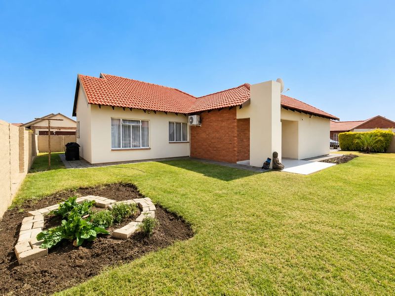 Rear view of the townhouse featuring a terracotta tiled roof, brick accents, a paved patio area, and a well-maintained garden.