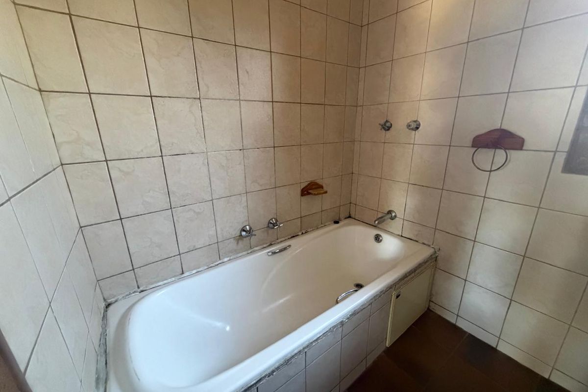 A functional bathroom featuring a built-in bathtub with wall-mounted fixtures and tiled wall finishes, requiring some maintenance to grout and sealant.