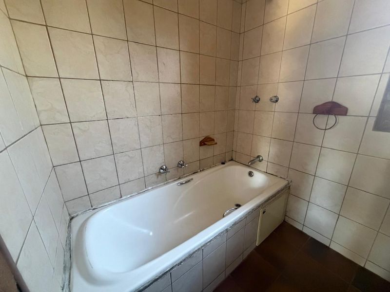 A functional bathroom featuring a built-in bathtub with wall-mounted fixtures and tiled wall finishes, requiring some maintenance to grout and sealant.