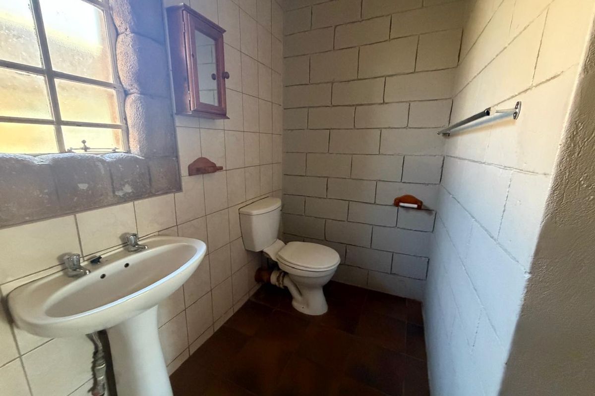A dated bathroom featuring a pedestal washbasin, toilet, and tiled finishes, offering potential for modernization and renovation.