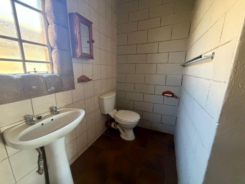 A dated bathroom featuring a pedestal washbasin, toilet, and tiled finishes, offering potential for modernization and renovation.