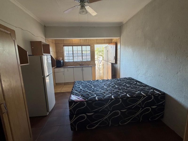 Open-plan studio space featuring a compact kitchenette with tiled backsplash and direct access to an exterior area.