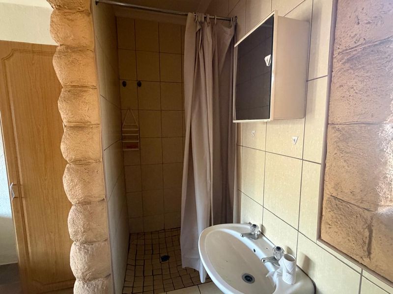 A compact bathroom featuring a shower enclosure, wall-mounted washbasin, and tiled finishes, offering potential for modernization and aesthetic improvement.