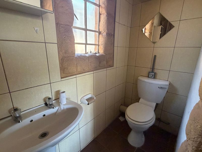 A compact bathroom featuring a pedestal basin, toilet, and stone-framed window, finished with dated ceramic wall tiles.