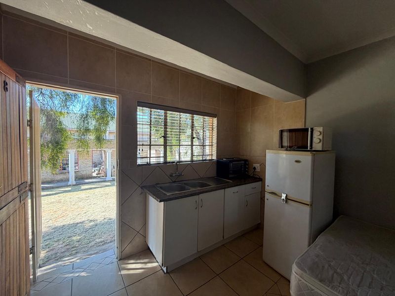 A functional kitchen area featuring built-in cabinetry, a double sink, tiled splashbacks, and direct access to the outdoor garden area.