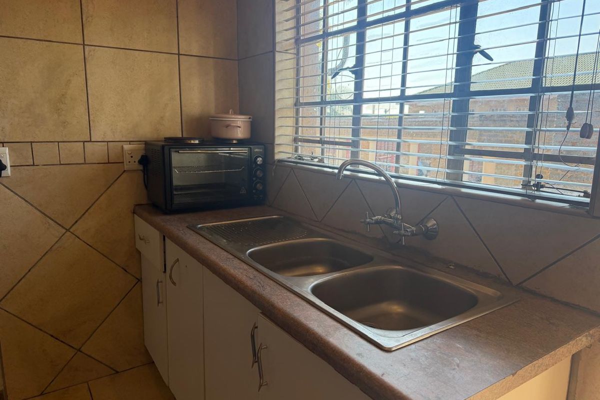 A functional kitchen area featuring a double stainless steel sink, laminate countertops, and tiled splashbacks with natural light from the window.