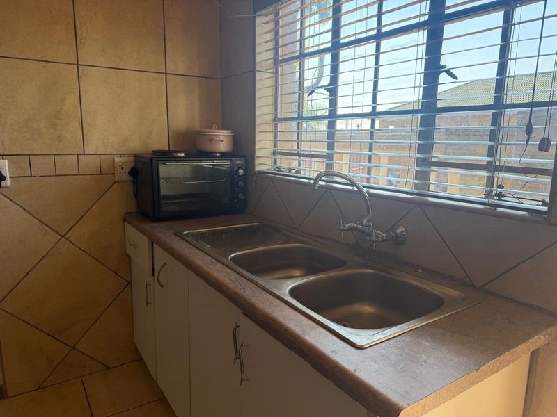 A functional kitchen area featuring a double stainless steel sink, laminate countertops, and tiled splashbacks with natural light from the window.