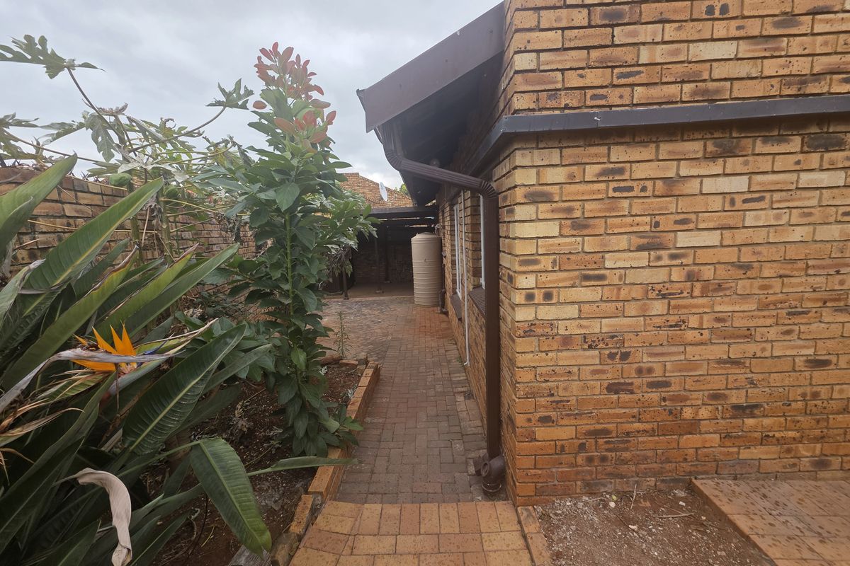 A side view of the townhouse exterior featuring face brick walls, a paved walkway, and a water storage tank in the rear garden area.